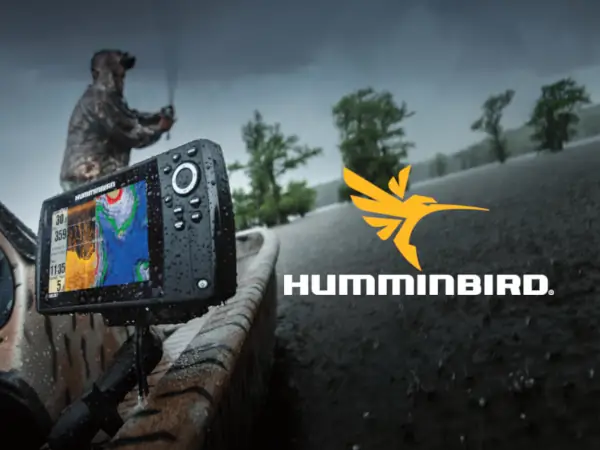 A person in rain gear fishes from a boat equipped with a Humminbird fish finder. The overcast sky and rain convey a rugged, adventurous tone.